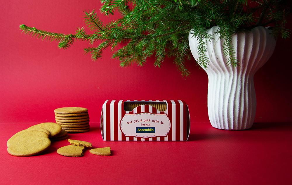 Pepparkaksask med egen design – exempel på röd standardask Röd- och vitrandig pepparkaksask med egen logotyp, pepparkakor och grankvist